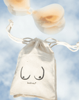 Product shot of Silicone Stick-on Bra with Boob-eez branded drawstring unbleached cotton muslin pouch laying flat against mirrored sky background showing how thin and weightless the Silicone Stick-on Bra is 